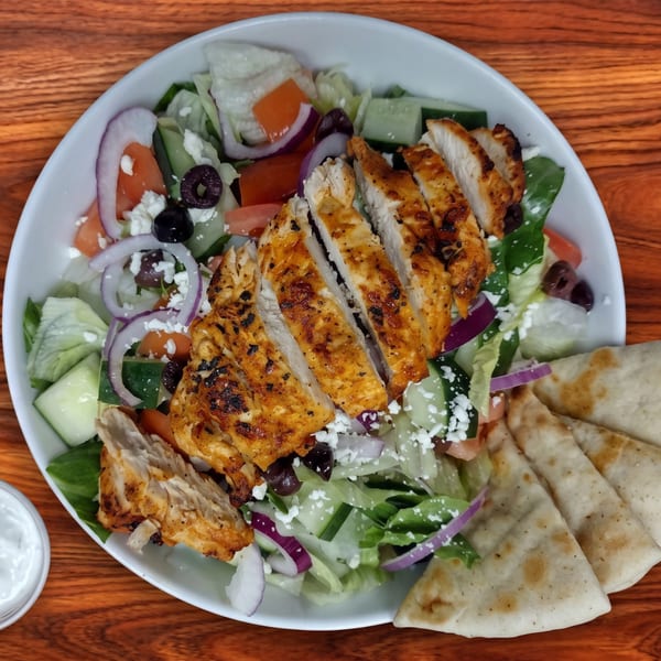 Grilled chicken salad with feta, olives, red onion, cucumber, and tomatoes, served with pita bread.