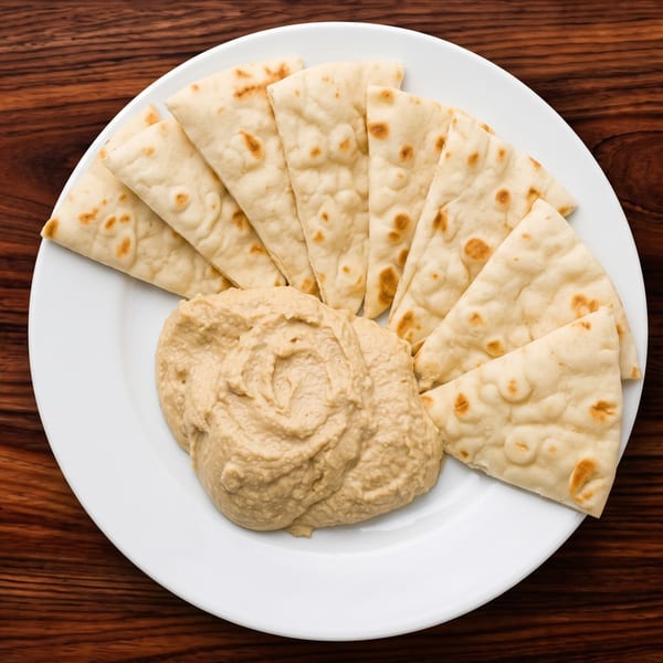 A white plate with a swirl of hummus and several triangular pieces of pita bread on a wooden table.