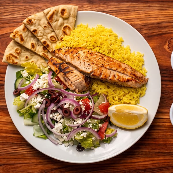 Grilled salmon with yellow rice, Greek salad, and pita bread on a white plate.